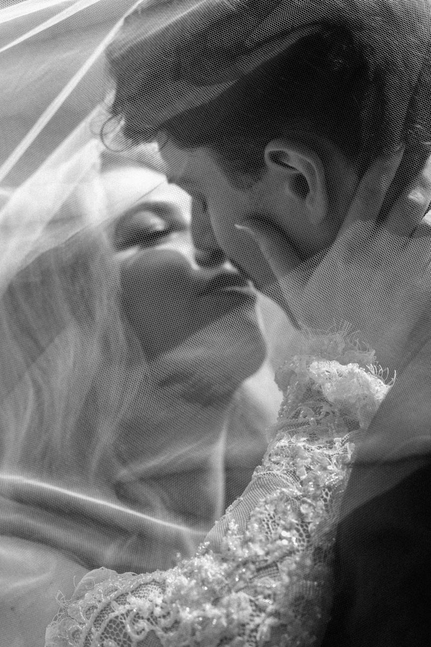 A close black and white view of a couple's kiss beneath a veil