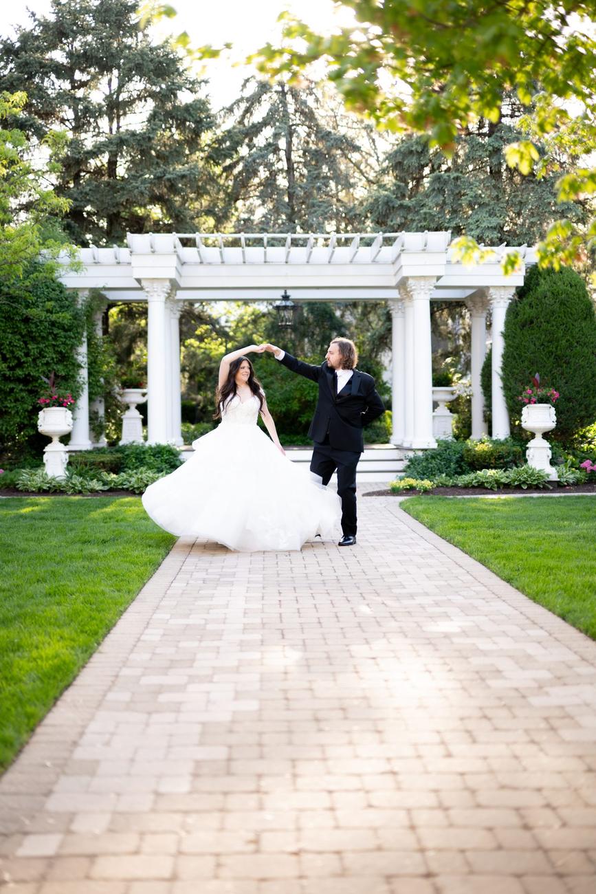 A couple dancing together on a garden path before a white pergola