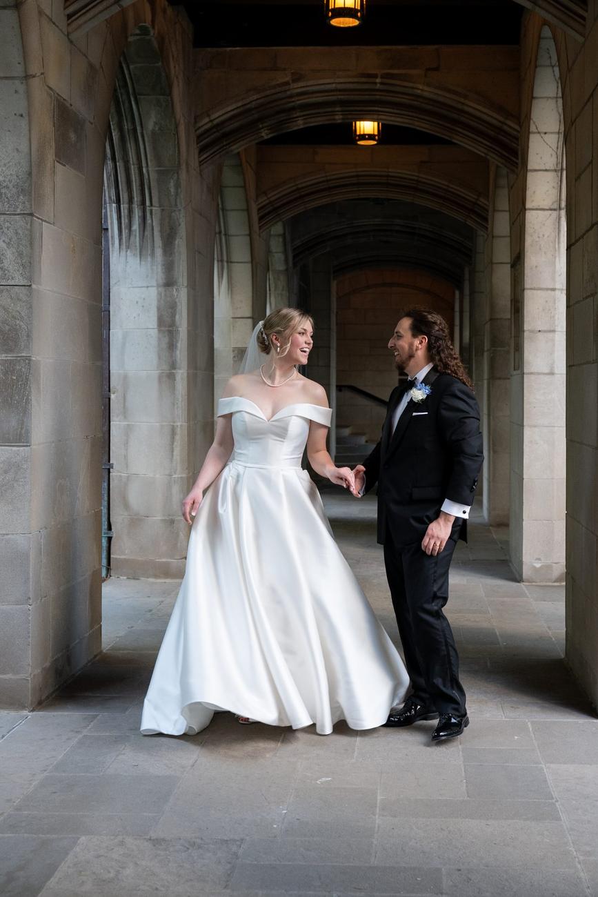 A couple walking side by side through a stone colonnade