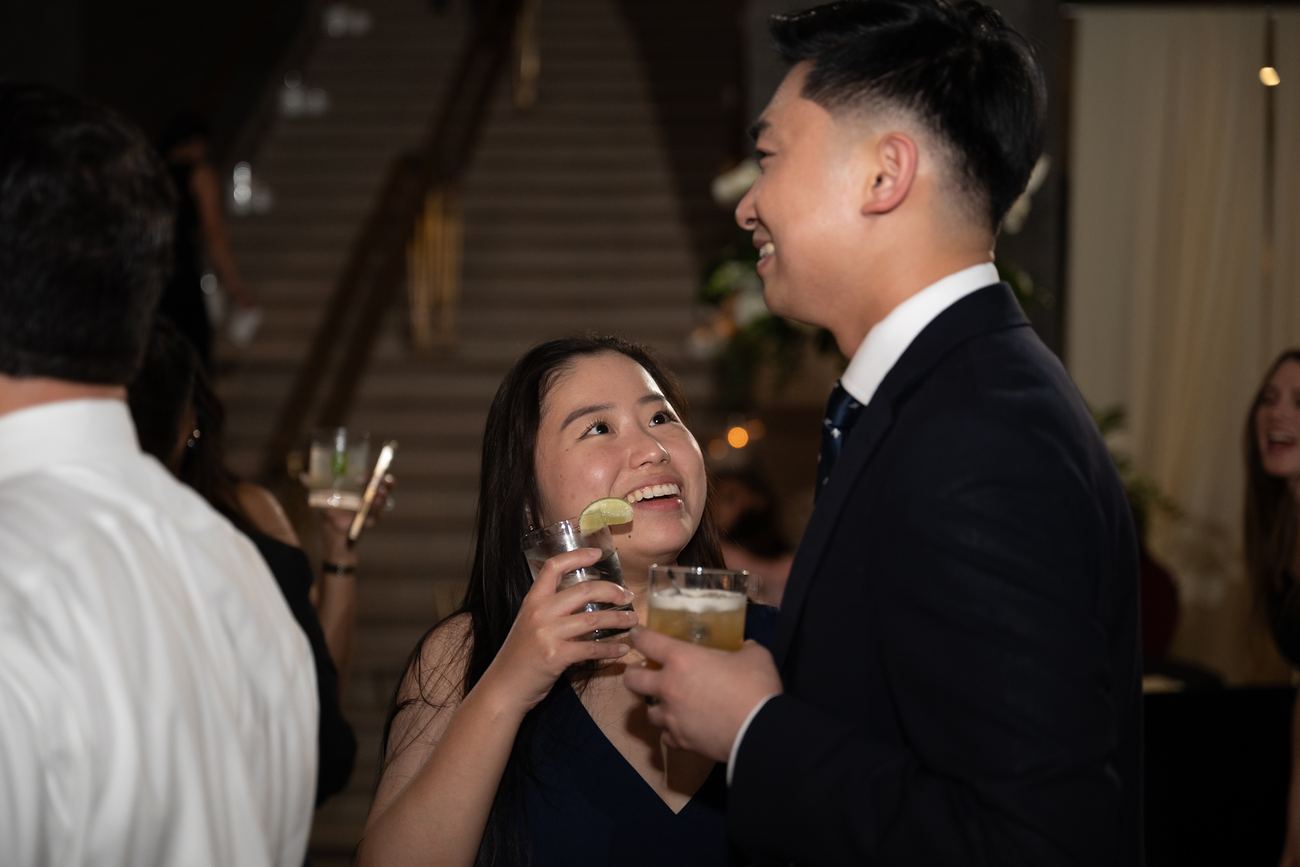 A couple laughing together, drinks in hand, at the reception