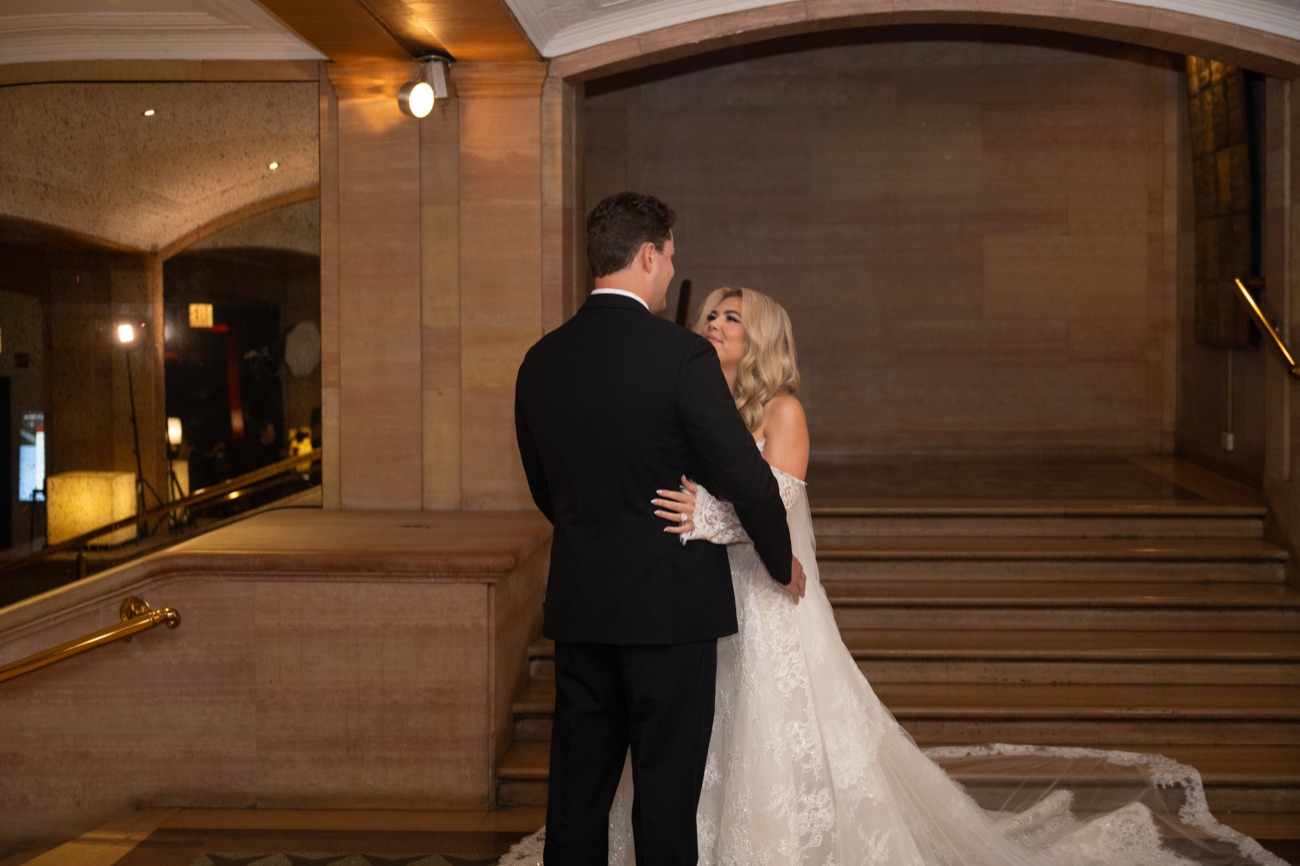 A groom embracing his bride at the foot of a grand staircase
