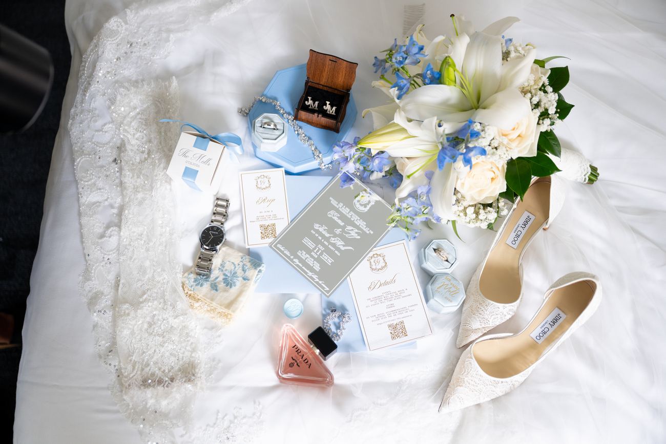Shoes, invitation suite, and jewelry arranged on a bed