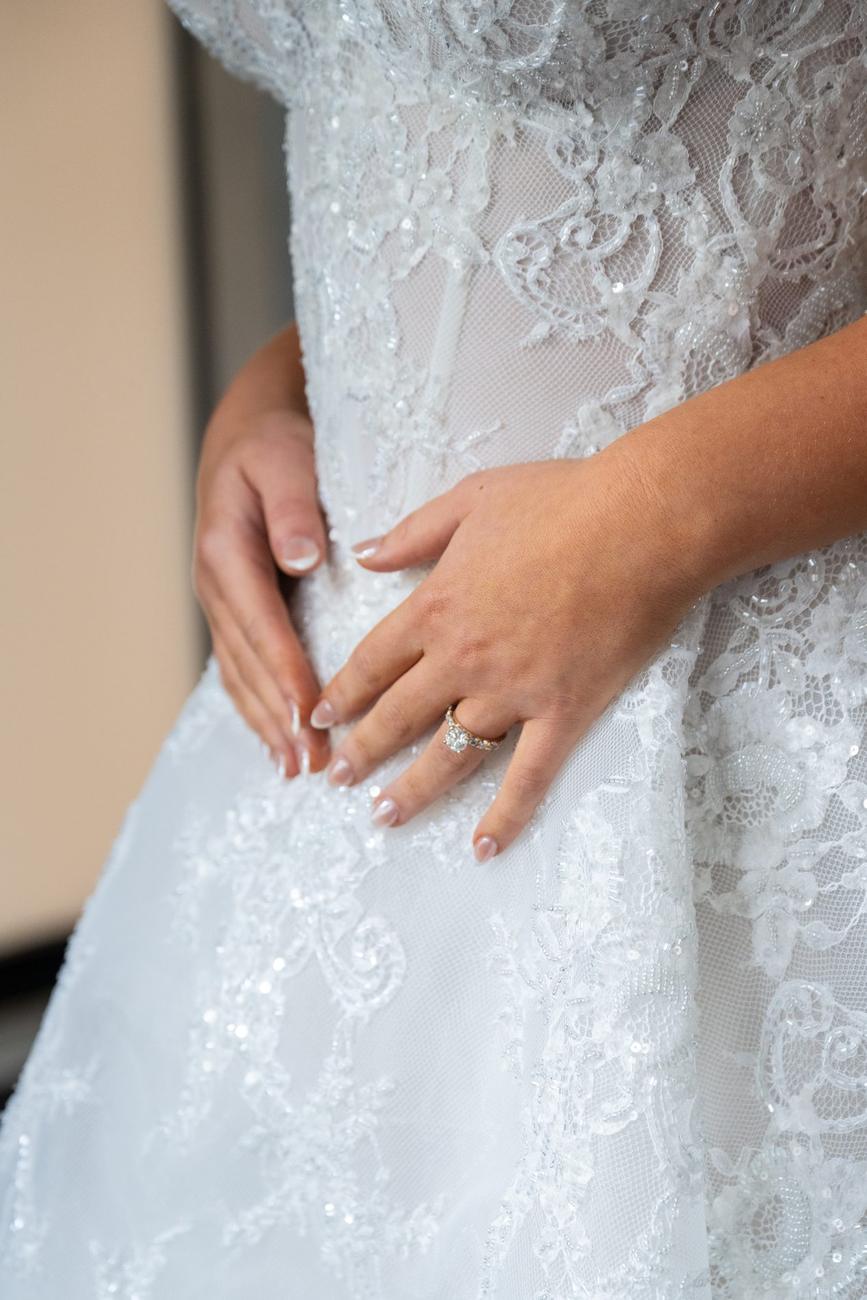 Hand adjusting lace on a wedding gown, engagement ring visible
