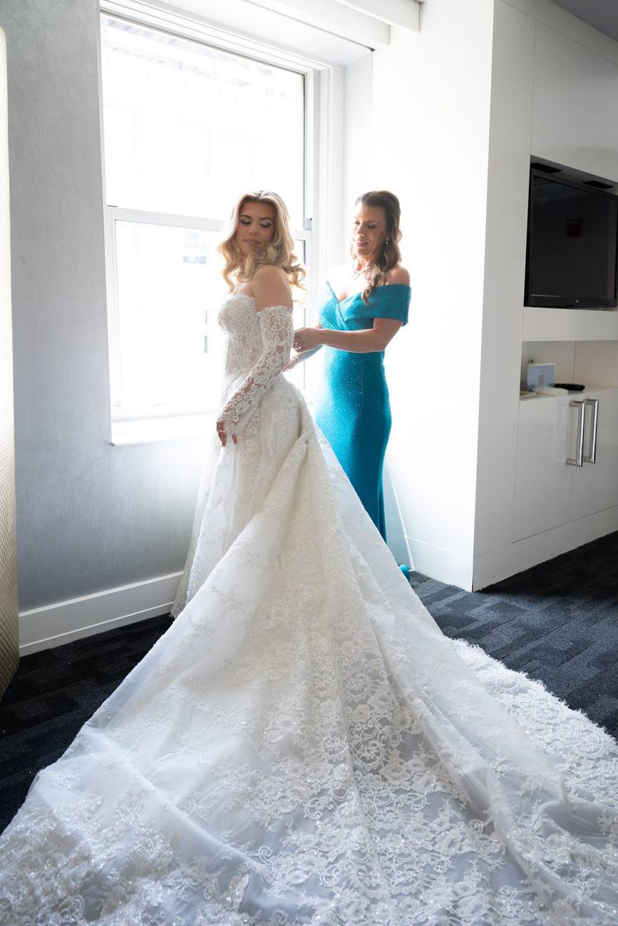 Bride in her gown by a bright window, bridesmaid in teal beside her
