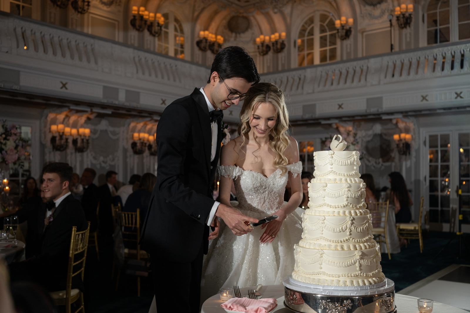 Bride and groom cutting the cake together, guests looking on