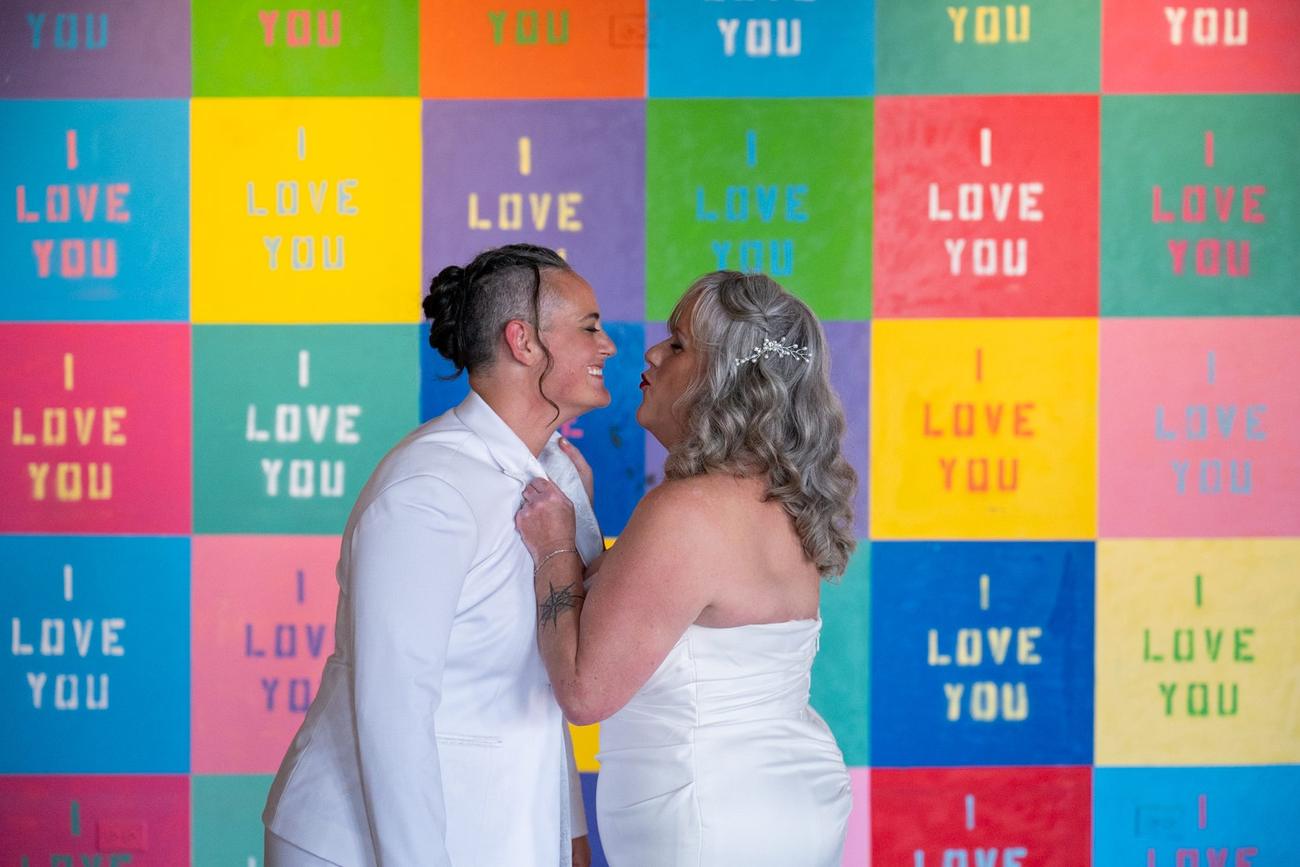 A couple embracing in front of a colorful photo booth backdrop
