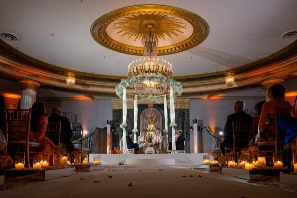 A couple seated before a sacred fire beneath a flower-draped mandap