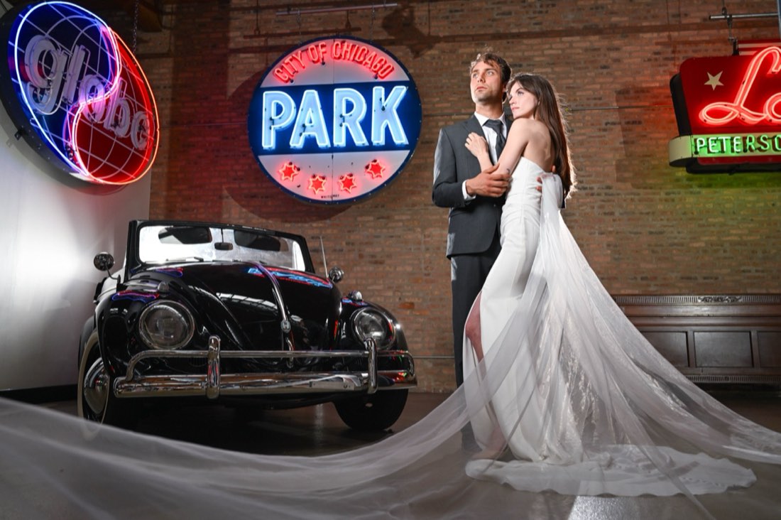 A couple posed beside a vintage convertible under vintage neon signs