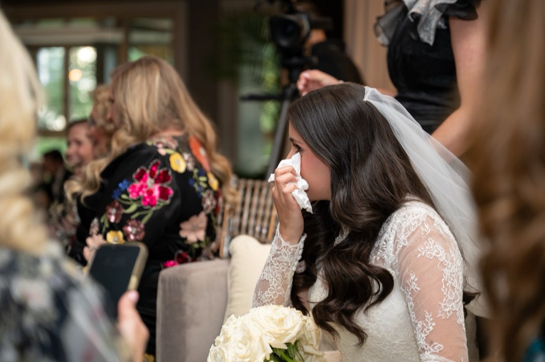 A bride wiping away tears, bouquet in hand, before the ceremony