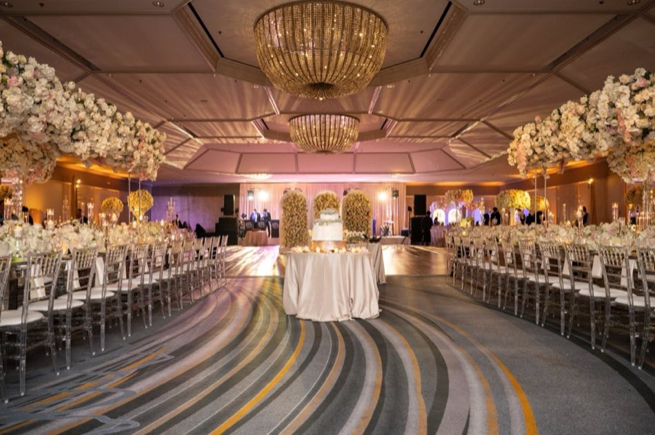 A grand reception ballroom set with floral arches and crystal chandeliers