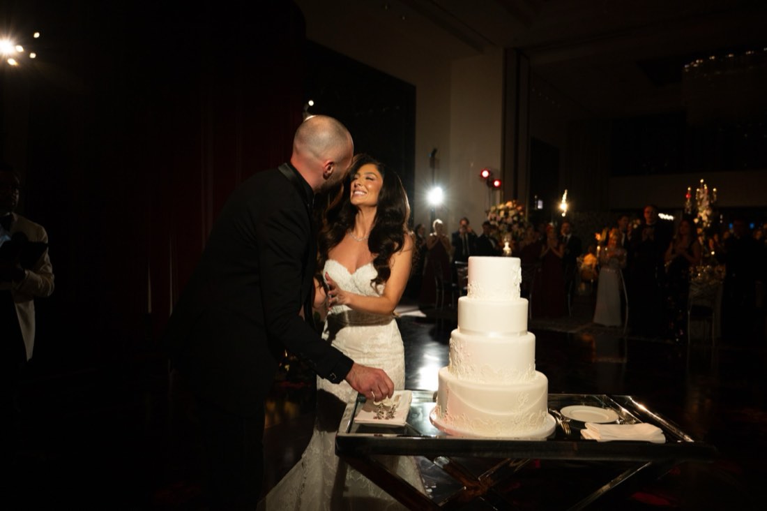 A couple cutting their wedding cake together in low light